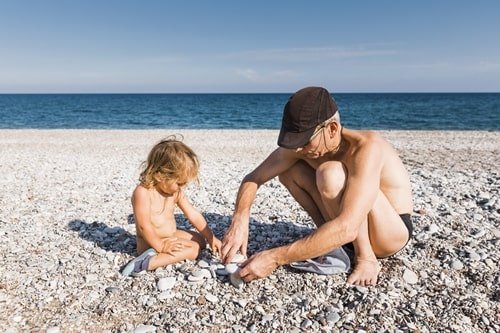 Vater oder Großvater spielt mit Enkelkind am Strand.