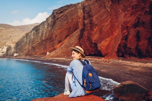 Junge Frau sitzt auf rotem Felsen am vor roten Steilklippen Red Beach