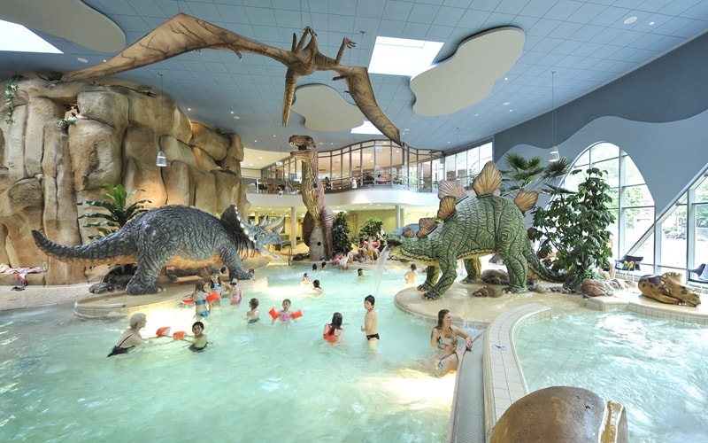Spielende Kinder und Dinosaurierfiguren an den Pools des Dinoland Festland.