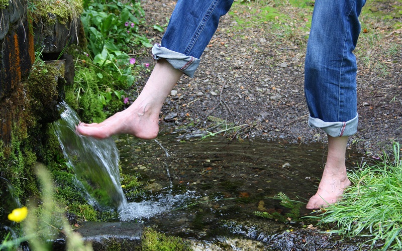 Eine Person wäscht sich die Füße an einer Quelle.