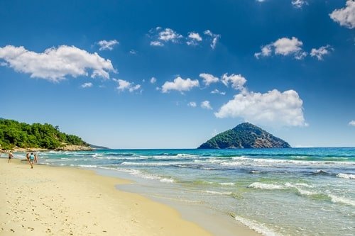 Feiner Sandstrand mit Strandspaziergängern und kleiner Insel im Hintergrund