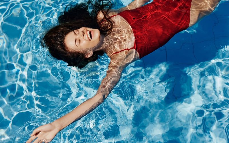 Eine Frau in rotem Badeanzug schwimmt lachend in einem Schwimmbecken.